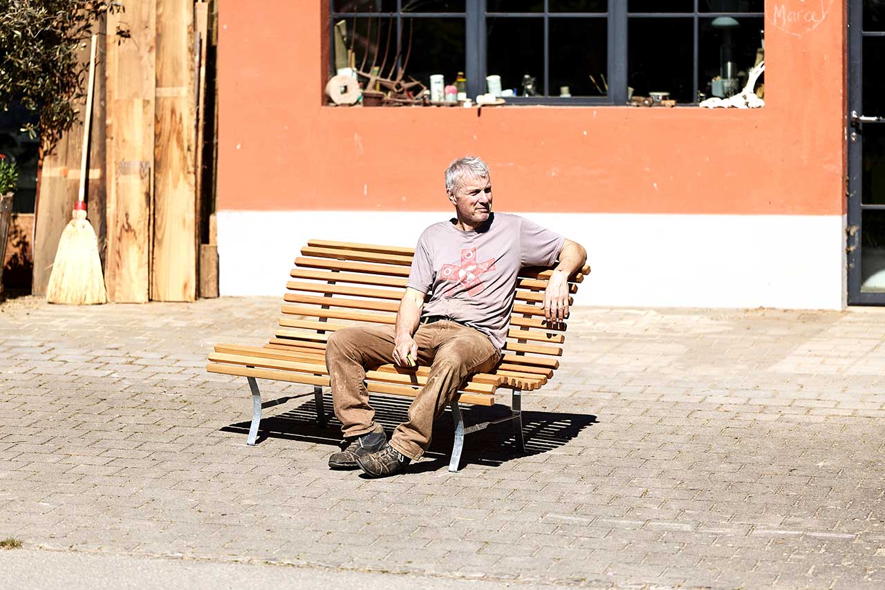 Marcel Pletscher auf der selbst erstellten Gartenbank vor seiner Werkstatt